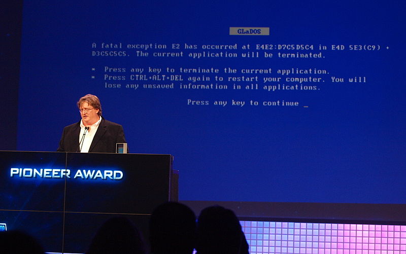 Gabe Newell faisant une présentation avec un écran bleu humoristique de la mort derrière lui